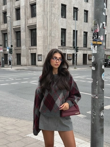 Close-up of argyle knit sweater with grey and burgundy diamonds and leather handbag