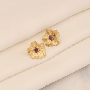 Nahaufnahme goldener Blumenohrstecker mit lilafarbenen Perlen auf weißem Seidenstoff