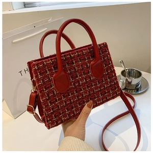 Detail of red tweed handbag with gold thread texture and faux leather handle on a table