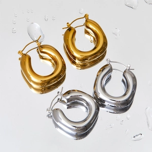 Detailed macro shot of gold and silver chunky oval hoop earrings on a wet mirror surface