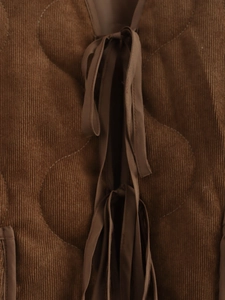 Detail van bruine corduroy stof met golfvormige wattering en striksluiting vooraan
