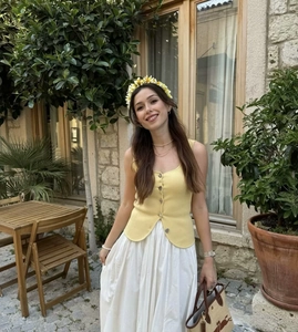 Outdoor shot of a yellow knit V-neck camisole top with decorative buttons for women