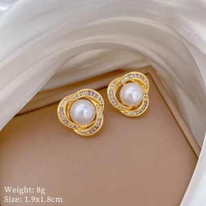 Macro view of gold pearl earrings with crystal bird nest spiral petals on satin