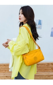 Side view of a yellow nylon crossbody bag with wide strap and decorative patch