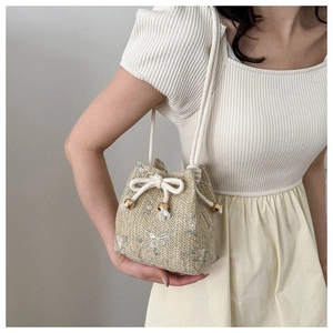 Détail d'un sac seau en paille tressée avec broderie florale et cordon en coton