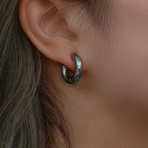 Macro shot of thick gunmetal grey stainless steel hoop earrings on a female model