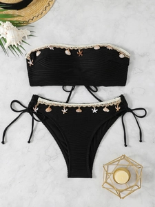 Detail of black ribbed bikini with shell and starfish pendants on marble background
