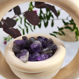 Close-up of polished purple amethyst stones in a natural wooden bowl frame