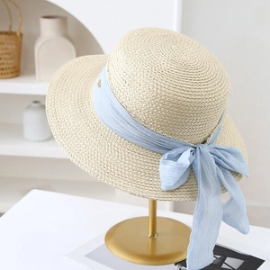 Detail of beige straw sun hat featuring a light blue chiffon ribbon and large bow design