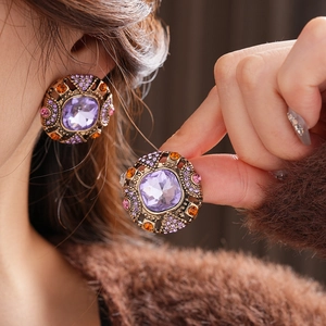 Close-up of vintage style square earrings featuring purple gemstones and orange crystals