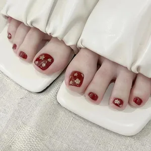 Macro shot of dark red press-on toenails with golden floral sequins on a white sandal