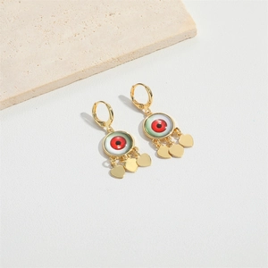 Close-up of golden evil eye earrings with red pupils and hanging gold heart charms