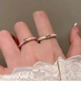 Close-up of pink and cream enamel rings with rectangular zircon on hand with lace