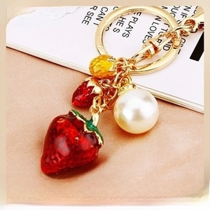 Detail of red strawberry keychain with large pearl accent and gold metal ring