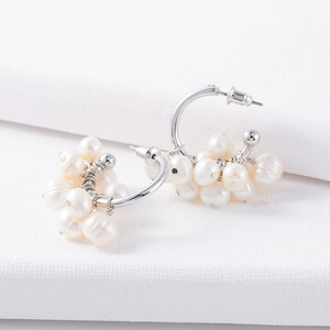 Macro shot of silver cluster earrings with natural white pearls on white fabric texture