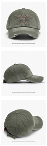 Detail of olive green washed cotton baseball cap with embroidered lettering and distressed holes