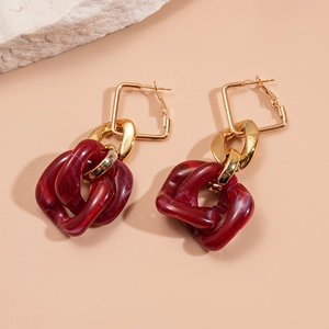 Detail of square gold metal earrings with red acrylic chain links on stone texture