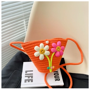 Detail der orangen Strohtasche mit lächelnden Blumenanhängern und Perlenverschluss-Deko