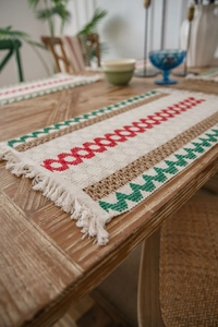 Close-up of woven table runner with red and green geometric patterns and boho tassels