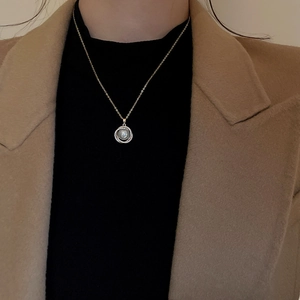 Détail d'un collier doré avec pendentif perle entouré de zircons porté par un mannequin