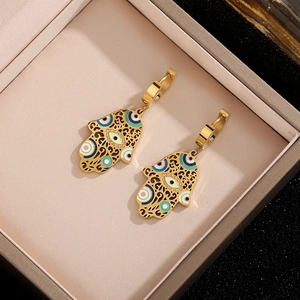 Gold Hamsa Hand earrings with blue enamel evil eye charm in a beige jewelry box