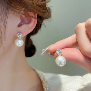 Detail of gold plated pearl earrings with sparkling cubic zirconia on a female model