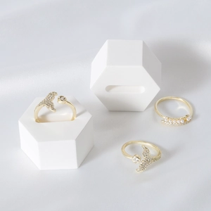 Minimalist gold fishtail and pearl rings set on a white hexagonal geometric jewelry stand