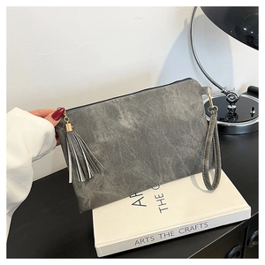 Detailed view of grey suede envelope bag featuring a stylish tassel and wrist strap