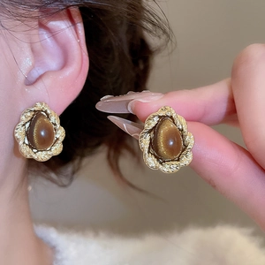 Detail of vintage gold twisted earrings with brown cat-eye stones on a model