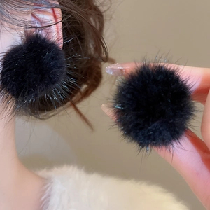 Gros plan détaillé sur des boucles d'oreilles pompons noirs avec texture en fausse fourrure