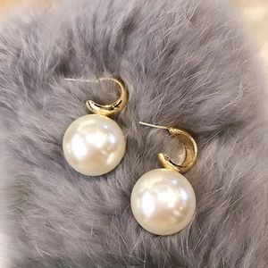 Detail shot of gold C-shaped earrings with large white pearls on grey fur background