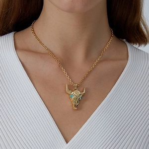 Gold bull skull pendant necklace with turquoise eyes on a woman wearing white top