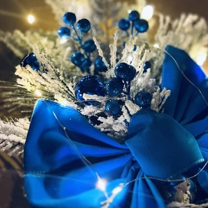 Macro detail of blue velvet bow, frosted pine needles and berries with LED lights