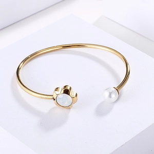 Detailed close-up of golden open bangle featuring a white flower and a lustrous pearl
