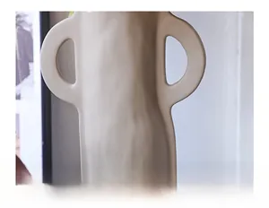 Detail of matte oat-colored ceramic vase with granular texture and dual handle design