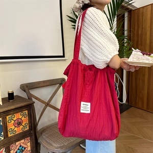 Detailed close-up of rose red pleated fabric tote bag with white logo label and soft texture