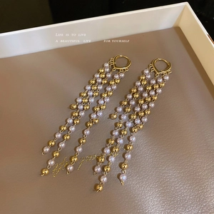 Elegant long tassel earrings with white pearls and gold beads on leather background