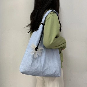 Close-up of light blue pleated canvas tote bag with white flower charm on female model