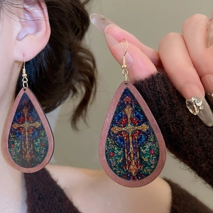 Close-up of teardrop wood earrings with colorful cross pattern on a female model