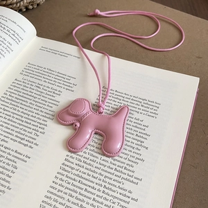 Détail du pendentif chiot rose avec couture fine sur un livre ouvert, accessoire mignon