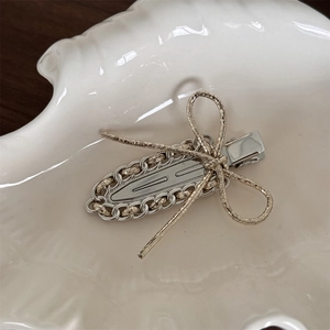 Detail of silver chain hair clip with a golden bow knot on a white ceramic shell plate