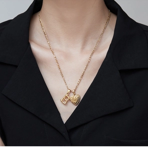 Detail of 18K gold-plated bamboo-style letter D and heart pendant on a Figaro chain