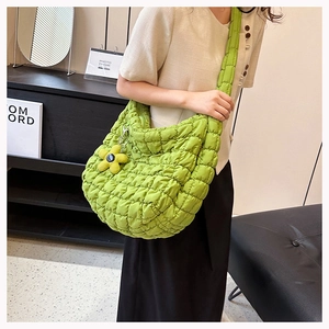 Detail of green quilted cloud tote bag with wide strap and yellow flower charm on model