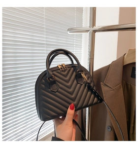 Detail of black quilted handbag with V-shaped stitching and golden metal zipper hardware