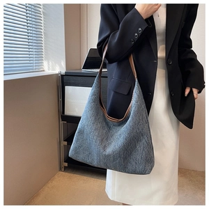 Blue denim hobo tote bag with brown leather shoulder strap shown on model's shoulder