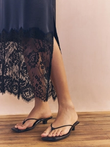 Close-up of elegant lace-trimmed satin skirt hem paired with black kitten heel sandals