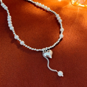 Close-up of pearl choker necklace featuring a heart pendant and long beaded tassel drop