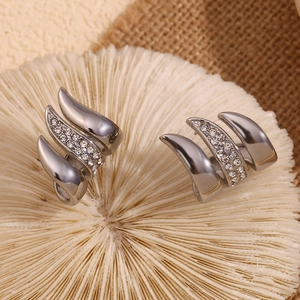 Close-up of three-prong geometric silver earrings with inset crystals on natural textures