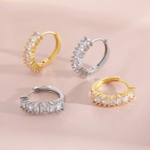 Gold and silver huggie earrings with square cubic zirconia stones on pink background