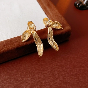 Macro shot of gold-plated ribbon earrings with brushed metal texture on red leather